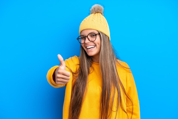 Young caucasian woman wearing winter clothes isolated on blue background with thumbs up because something good has happened