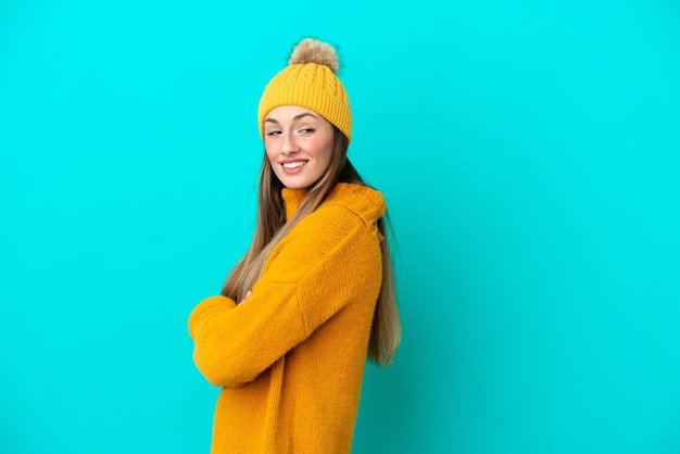 Young caucasian woman wearing winter jacket isolated on blue background with arms crossed and happy