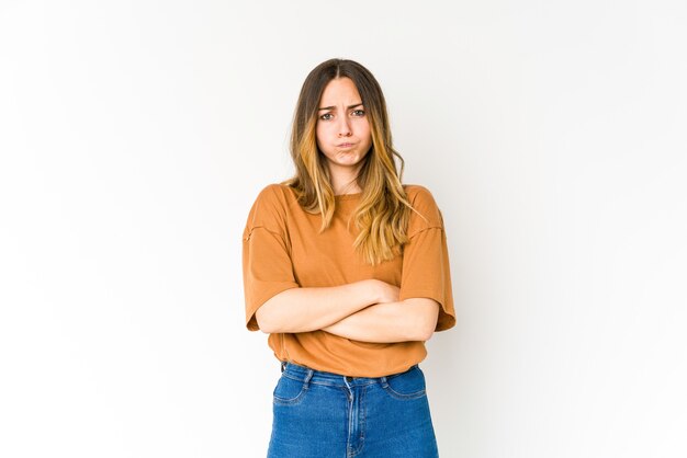 Young caucasian woman on white blows cheeks, has tired expression. Facial expression concept.