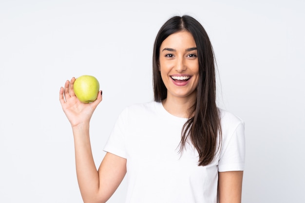 Young caucasian woman on white wall with an apple and happy