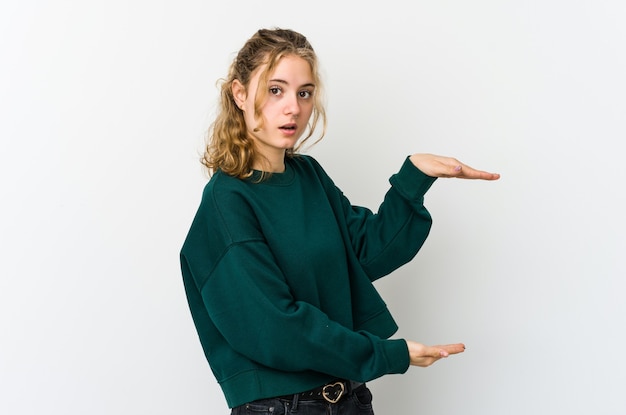 Young caucasian woman on white wallshocked and amazed holding a copy space between hands.