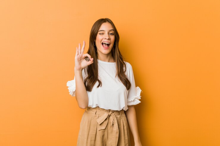Photo 若い白人女性は目をまばたきし、手でいいジェスチャーを保持します。