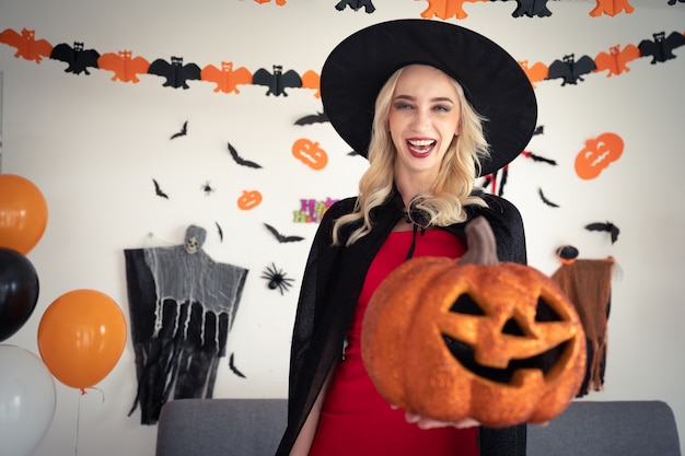 Young caucasian woman in witch clothing holding pumpkin party at home