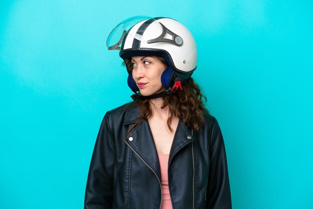 Фото Молодая кавказская женщина в мотоциклетном шлеме на синем фоне смотрит в сторону