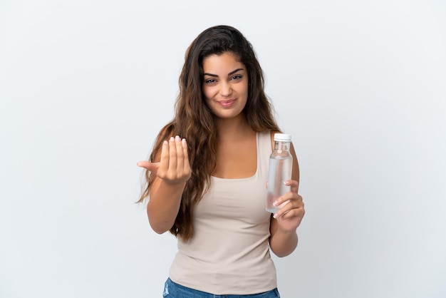 Young caucasian woman with a bottle of water isolated on white background inviting to come with hand. Happy that you came