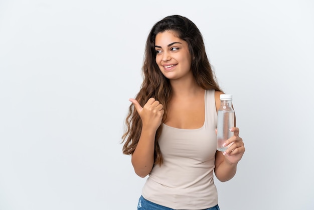 Young caucasian woman with a bottle of water isolated on white background pointing to the side to present a product