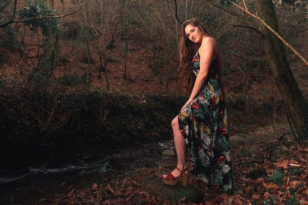 Young caucasian woman with a colorful dress in the middle of the forest next to a little river