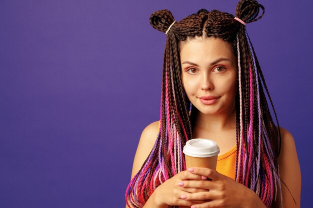 Young caucasian woman with colorful long cornrows holding a cup of coffee on purple