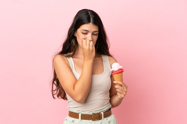 Young caucasian woman with a cornet ice cream isolated on pink background having doubts