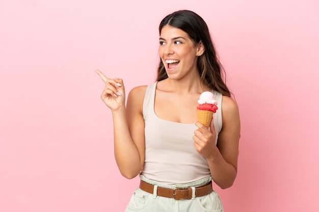 Young caucasian woman with a cornet ice cream isolated on pink background intending to realizes the solution while lifting a finger up