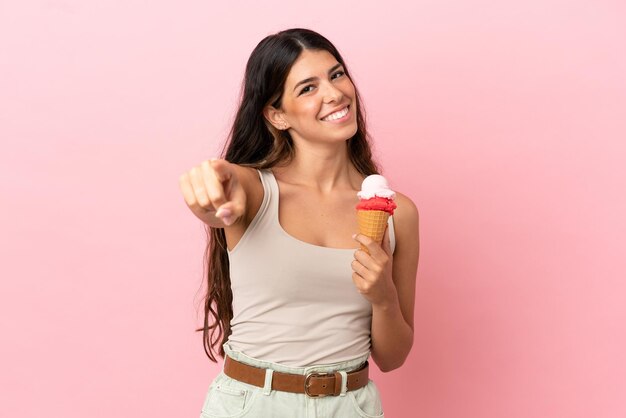 Young caucasian woman with a cornet ice cream isolated on pink background pointing front with happy expression