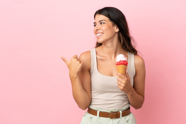 Young caucasian woman with a cornet ice cream isolated on pink background pointing to the side to present a product