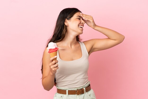 Young caucasian woman with a cornet ice cream isolated on pink background smiling a lot