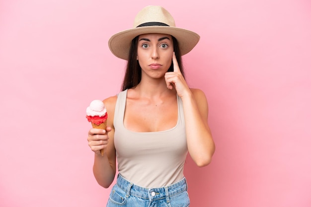 Giovane donna caucasica con un gelato alla cornetta isolato su sfondo rosa pensando a un'idea