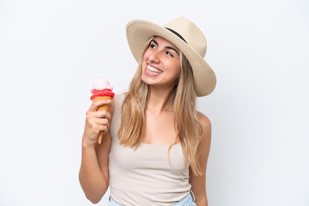 Giovane donna caucasica con un gelato alla cornetta isolato su sfondo bianco guardando in alto mentre sorride