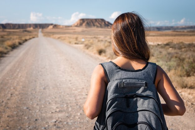 Photo young caucasian woman with a grey backpack walking in the middle of a dessert at bardenas, navarre, basque country.