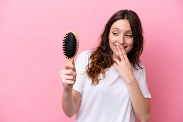 Young caucasian woman with hair comb isolated on pink background with surprise and shocked facial expression