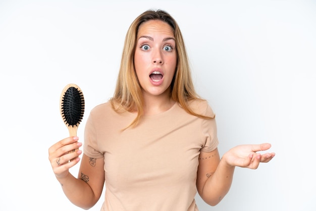 Young caucasian woman with hair comb isolated on white background with shocked facial expression