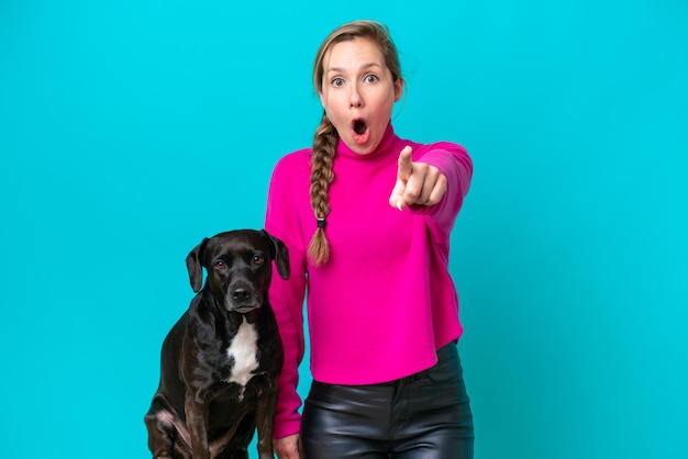 Young caucasian woman with her dog isolated on blue background surprised and pointing front