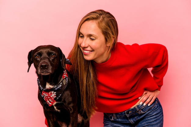 Young caucasian woman with her dog isolated on pink background