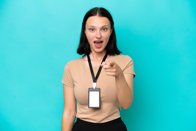 Photo young caucasian woman with id card isolated on blue background surprised and pointing front