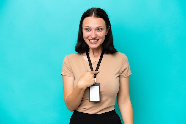 Young caucasian woman with ID card isolated on blue background with surprise facial expression