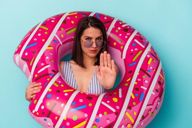 파란색 배경에 풍선 도넛을 들고 있는 젊은 백인 여성이 당신을 방해하는 정지 신호를 보여주는 뻗은 손
