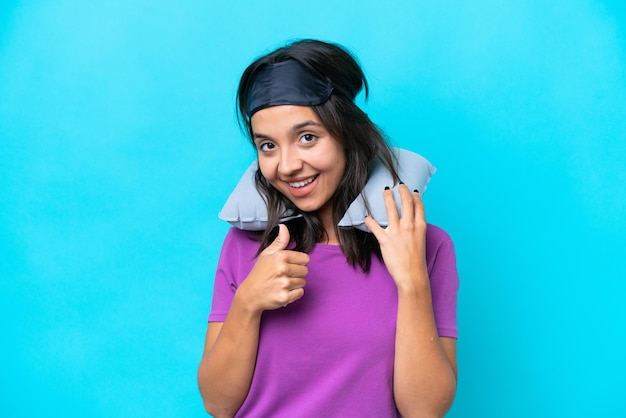 Photo young caucasian woman with inflatable travel pillow isolated on blue background giving a thumbs up gesture