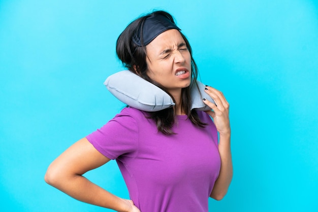 Young caucasian woman with inflatable travel pillow isolated on blue background suffering from backache for having made an effort