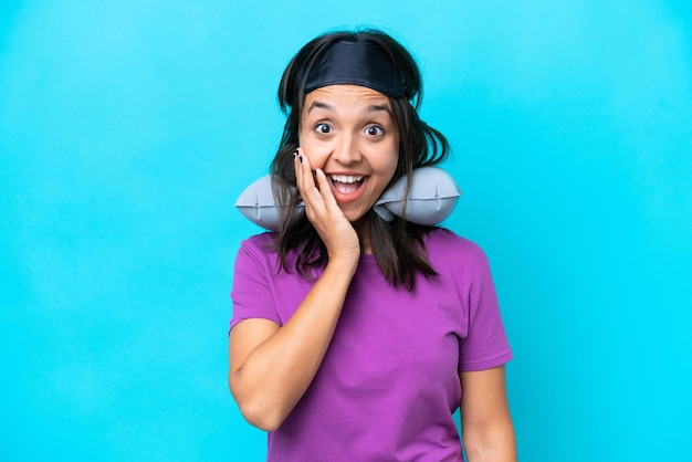 Young caucasian woman with inflatable travel pillow isolated on blue background with surprise and shocked facial expression