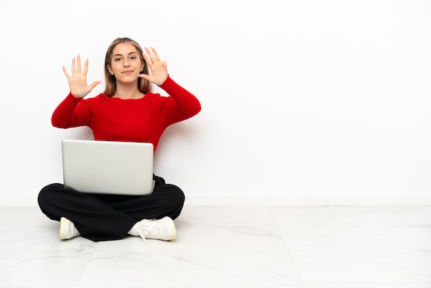 Young caucasian woman with a laptop sitting on the floor counting nine with fingers