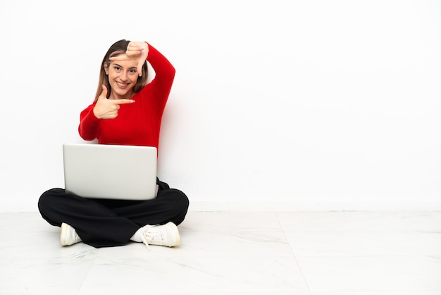 Young caucasian woman with a laptop sitting on the floor focusing face. Framing symbol