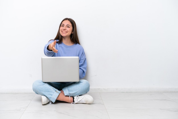 Young caucasian woman with laptop sitting on the floor isolated on white background shaking hands for closing a good deal