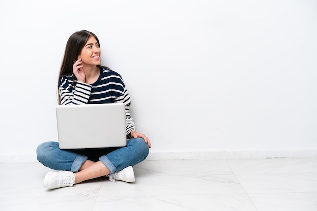 Young caucasian woman with a laptop sitting on the floor isolated on white background thinking an idea