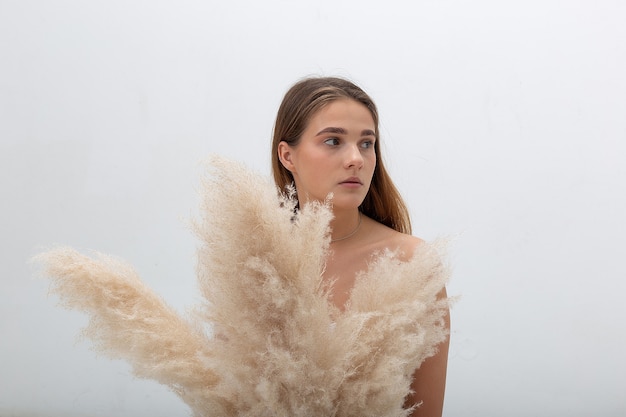 Young caucasian woman with long hair posing at studio, holding pampas grass