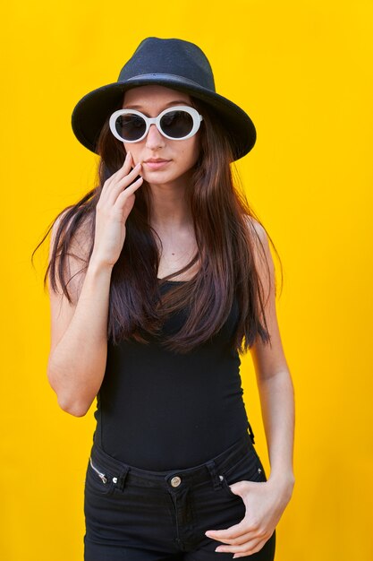 young caucasian woman with long hair sunglasses, black hat, tank top and black pants, hand over face