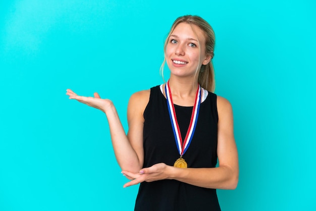 Young caucasian woman with medals isolated on blue background extending hands to the side for inviting to come