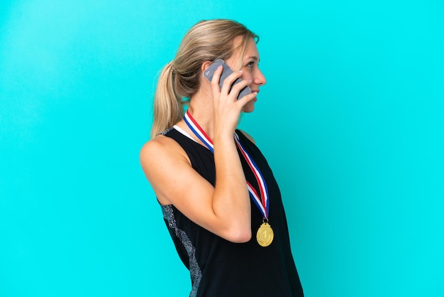 Молодая кавказская женщина с медалями на синем фоне ведет с кем-то разговор по мобильному телефону