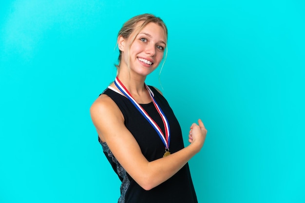 Young caucasian woman with medals isolated on blue background pointing back