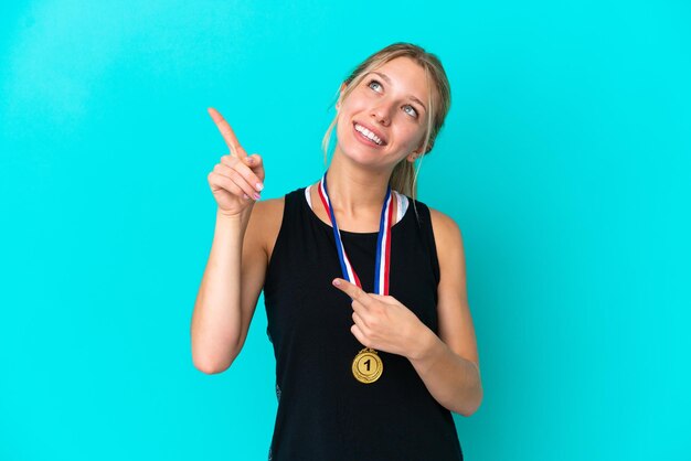 검지 손가락으로 가리키는 파란색 배경에 격리된 메달을 가진 젊은 백인 여성