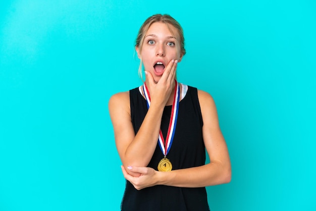 Young caucasian woman with medals isolated on blue background surprised and shocked while looking right