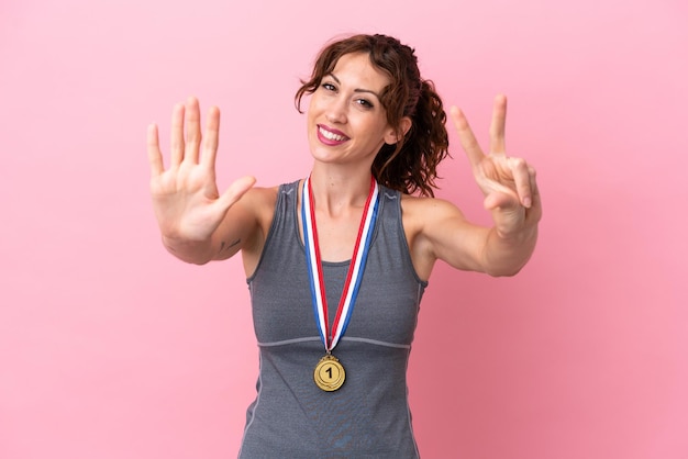 Young caucasian woman with medals isolated on pink background counting eight with fingers