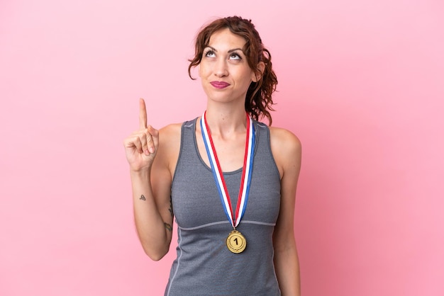 Young caucasian woman with medals isolated on pink background pointing with the index finger a great idea