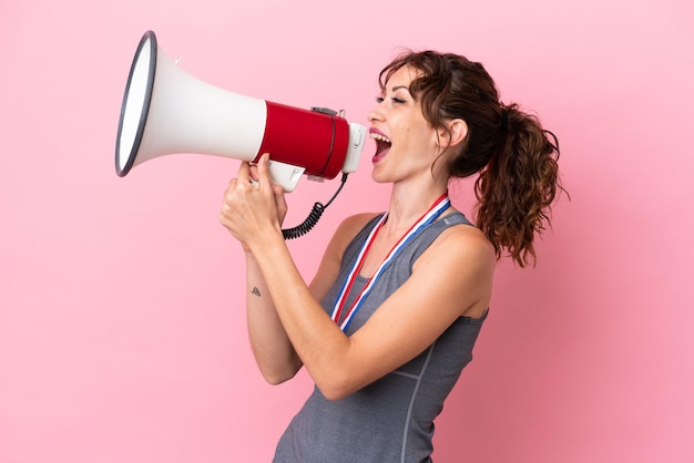 Young caucasian woman with medals isolated on pink background shouting through a megaphone