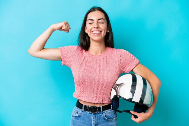 Young caucasian woman with a motorcycle helmet isolated on blue background doing strong gesture