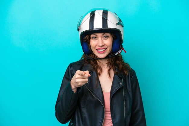 Young caucasian woman with a motorcycle helmet isolated on blue\
background surprised and pointing front