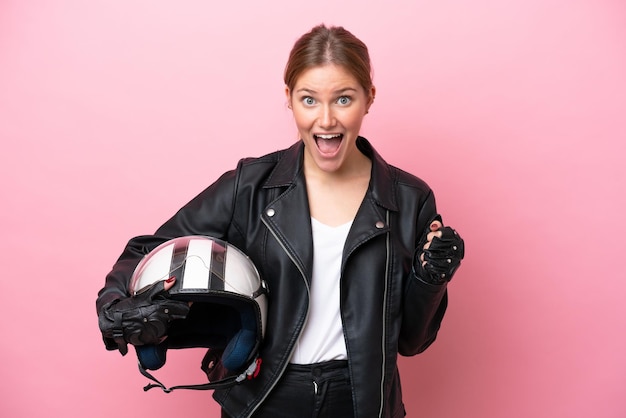 Giovane donna caucasica con un casco da motociclista isolato su sfondo rosa che celebra una vittoria in posizione di vincitore