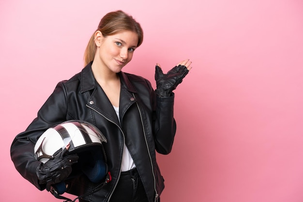 Young caucasian woman with a motorcycle helmet isolated on pink background extending hands to the side for inviting to come