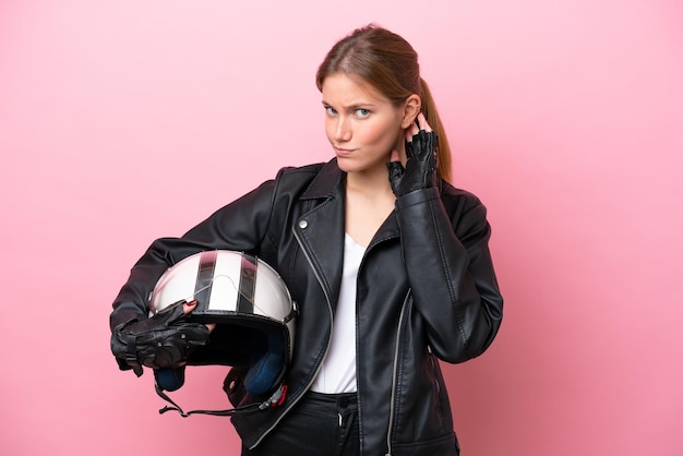 Young caucasian woman with a motorcycle helmet isolated on pink background having doubts