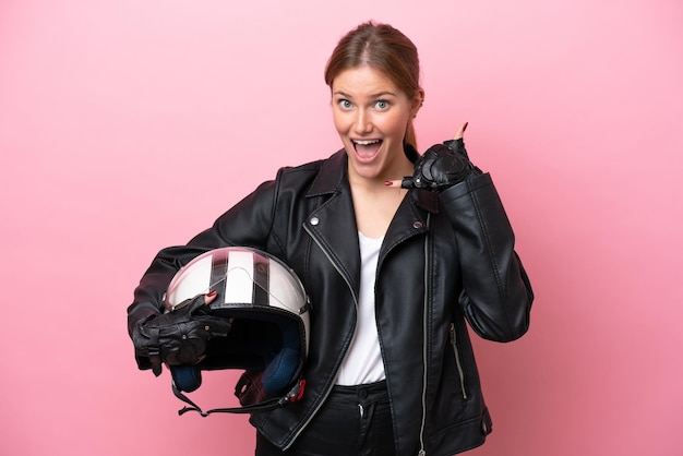 Young caucasian woman with a motorcycle helmet isolated on pink background making phone gesture Call me back sign